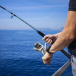 Close-up of man's hand holding fishing rod in the sea, man fishing. Fishing rod with a spinning reel in the hands of a fisherman.